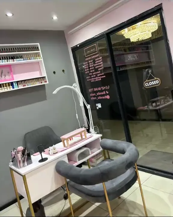 The studio: a white manicure desk with a pink cushion, grey velvet chair and a wall of polish
